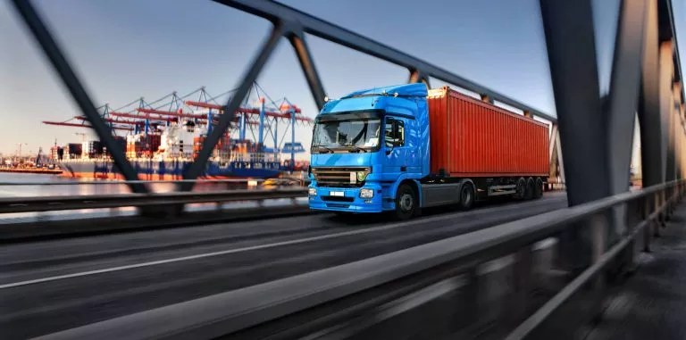 LKW fährt über Hafenbrücke mit Kränen im Hintergrund