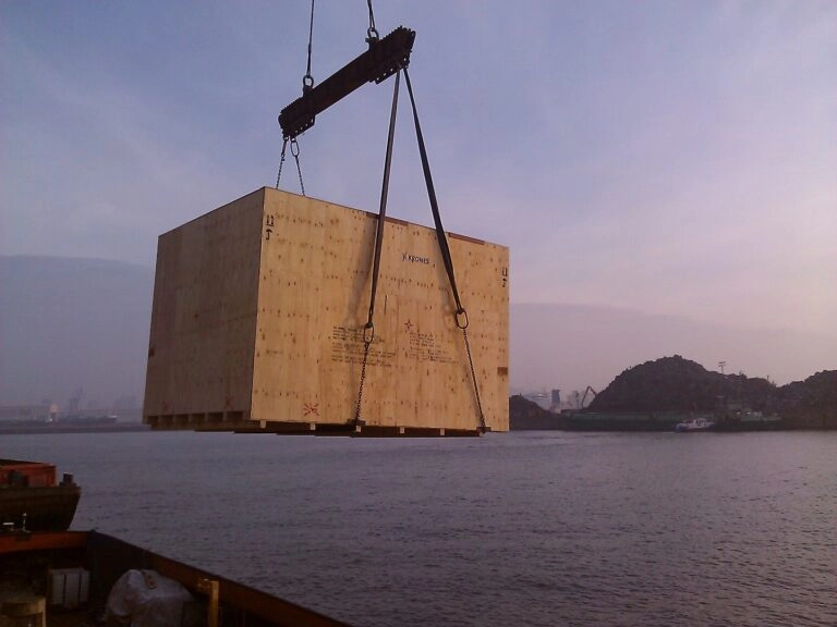 Eine Holzverpackung wird mit einem Kran auf ein Frachtschiff gehoben.