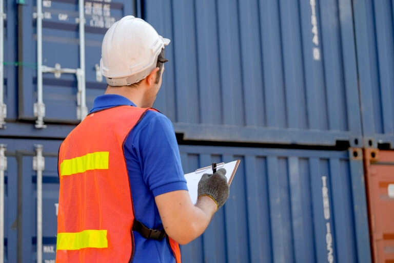 Ein Lagermitarbeiter vor Containern notiert auf ein Klemmbrett Informationen für die Transportorganisation.